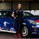 Rally driver Catie Munnings poses next to a car.